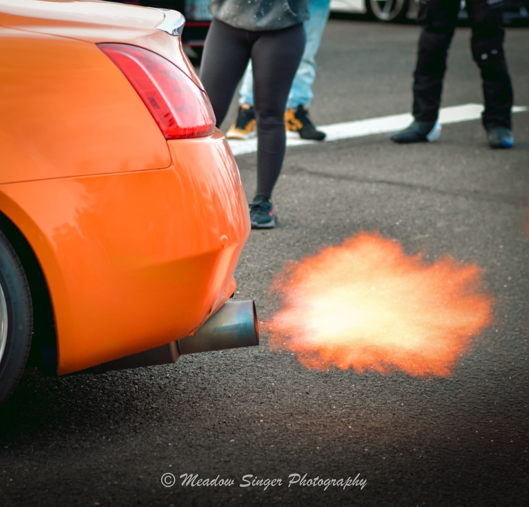 Flames shooting from the exhaust of an orange car at a show