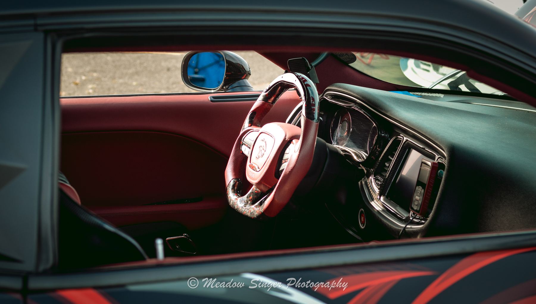 A red leather steering wheel and dash seen through a car window