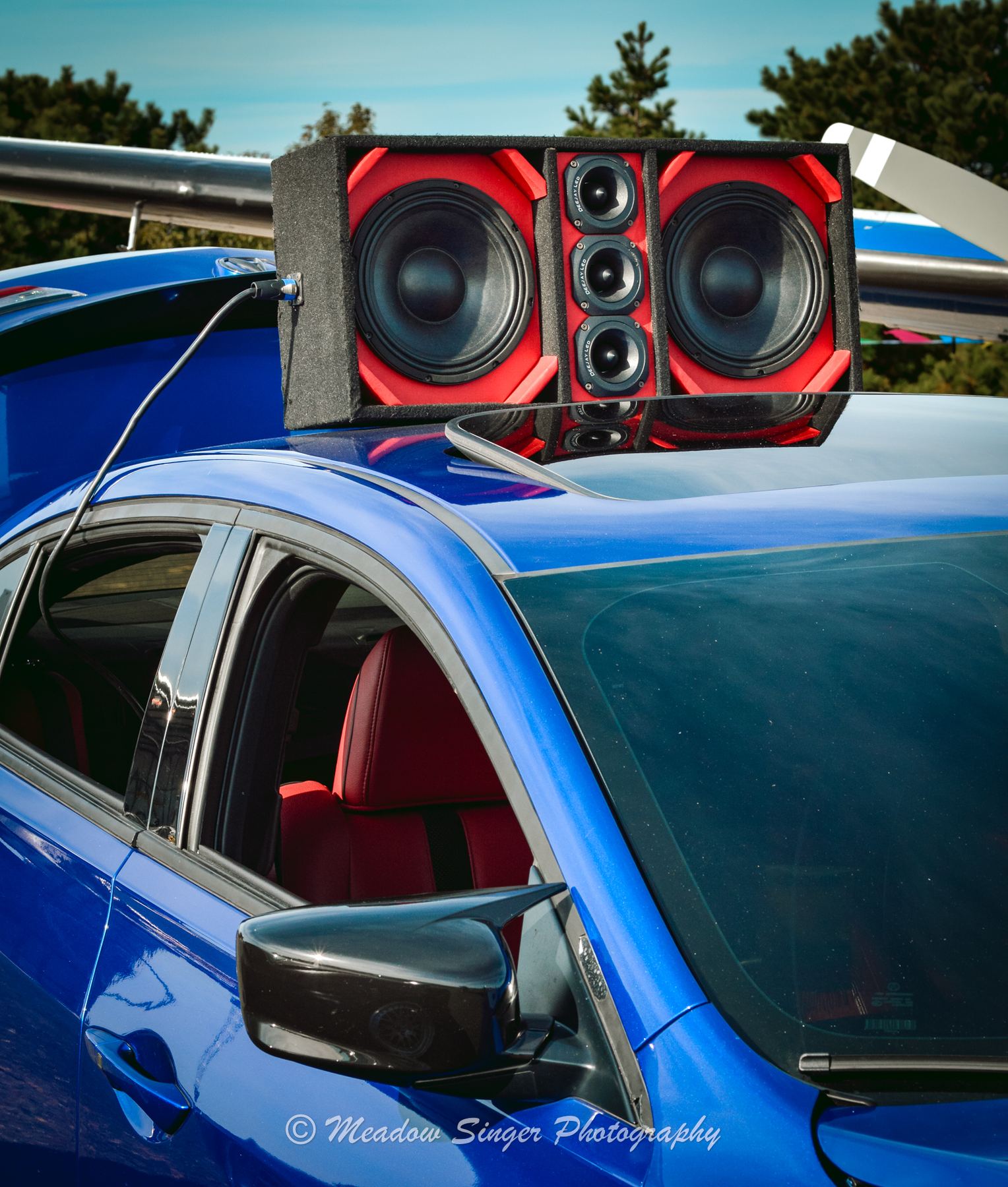 A red speaker box mounted on the roof of a blue car