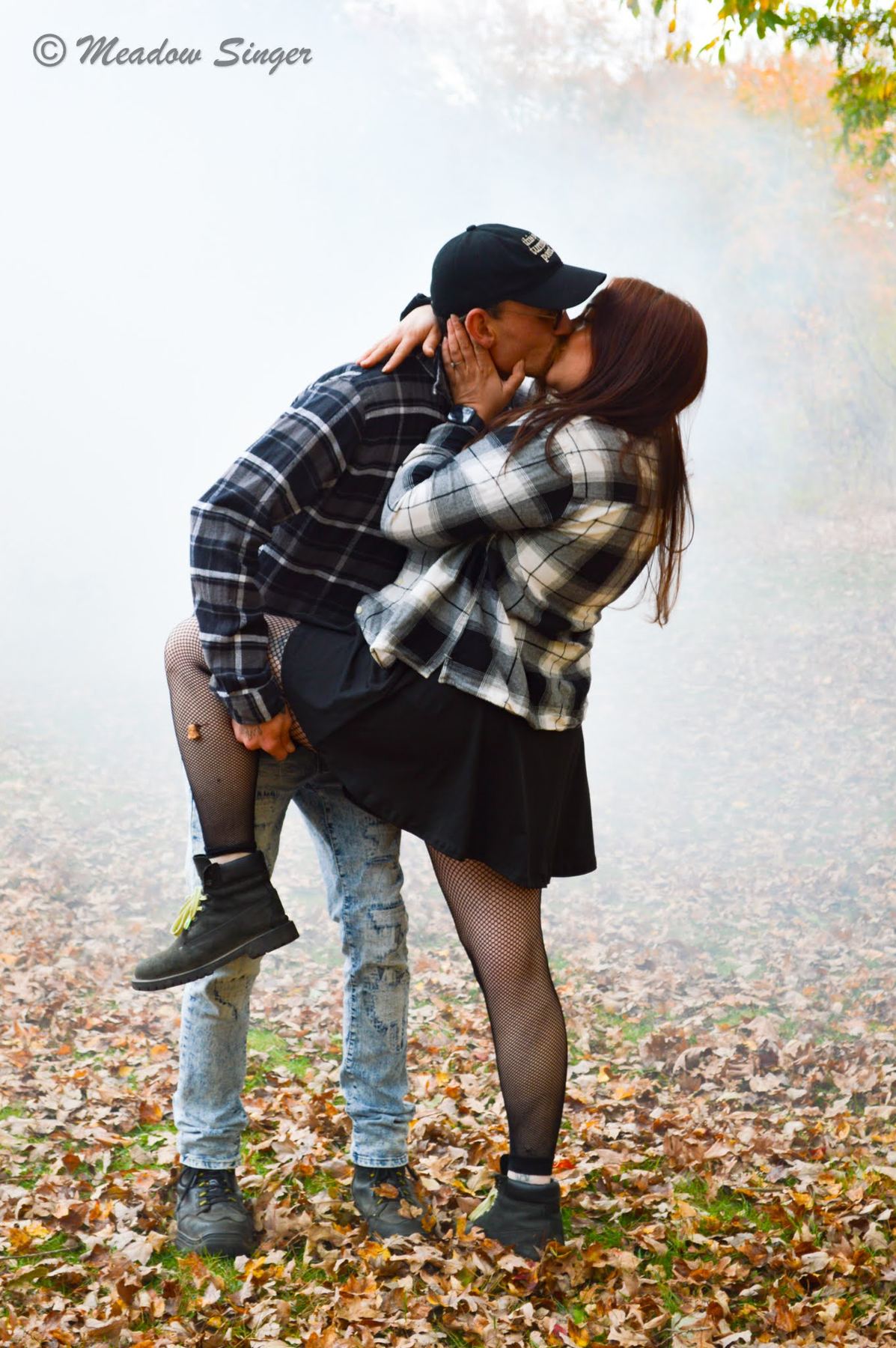 A couple in flannel kissing in fog among fallen leaves