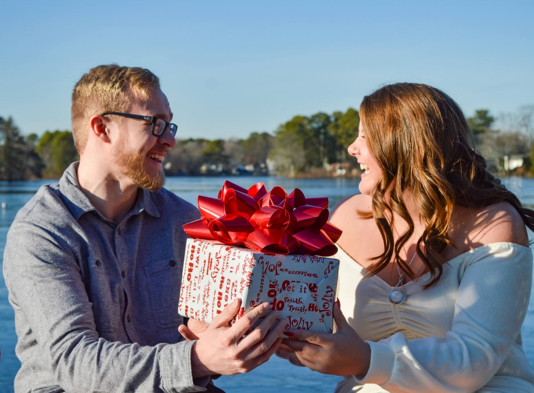 A couple by a lake, one handing the other a wrapped gift