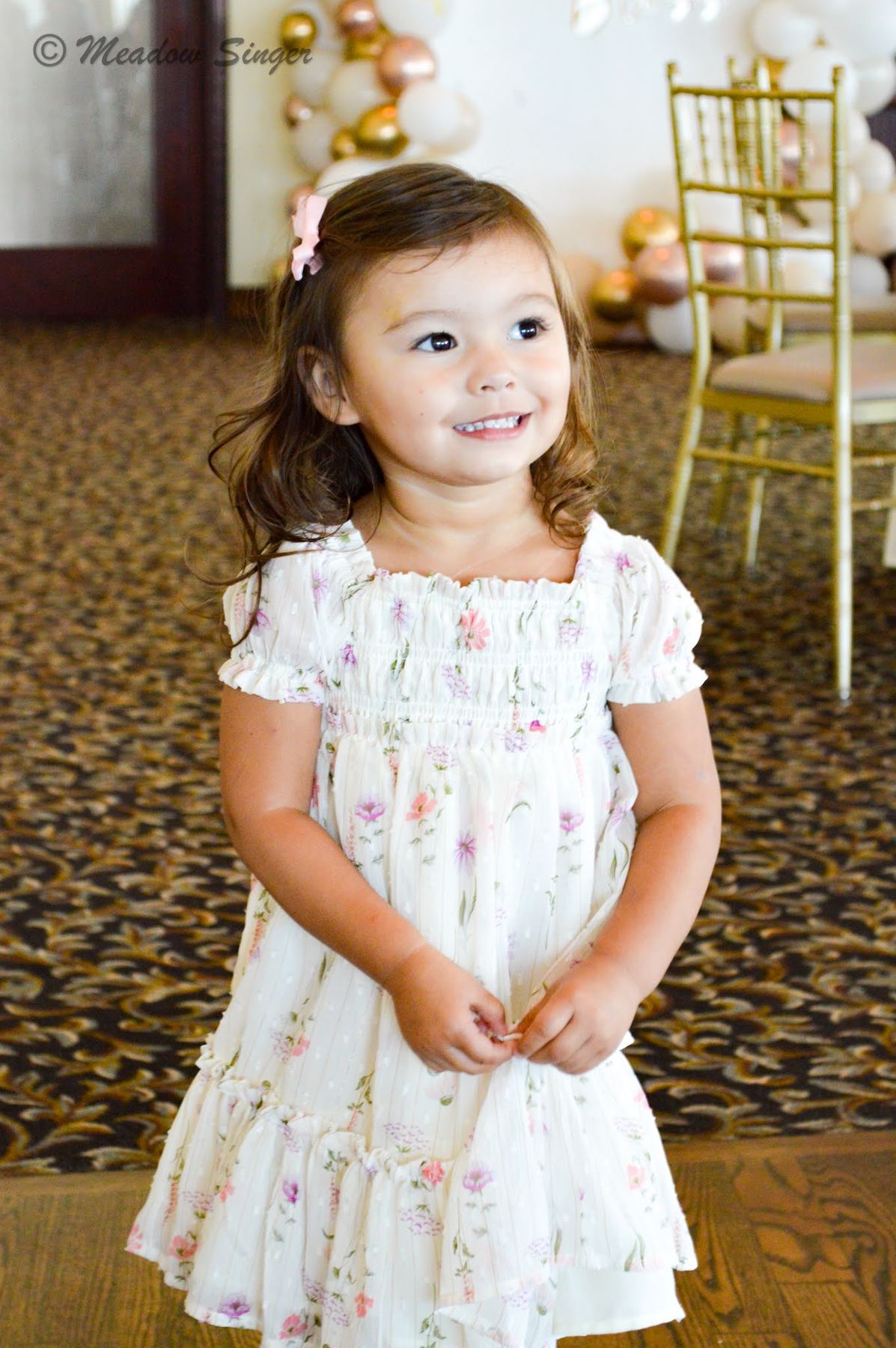 A little girl in a floral dress smiling at a party