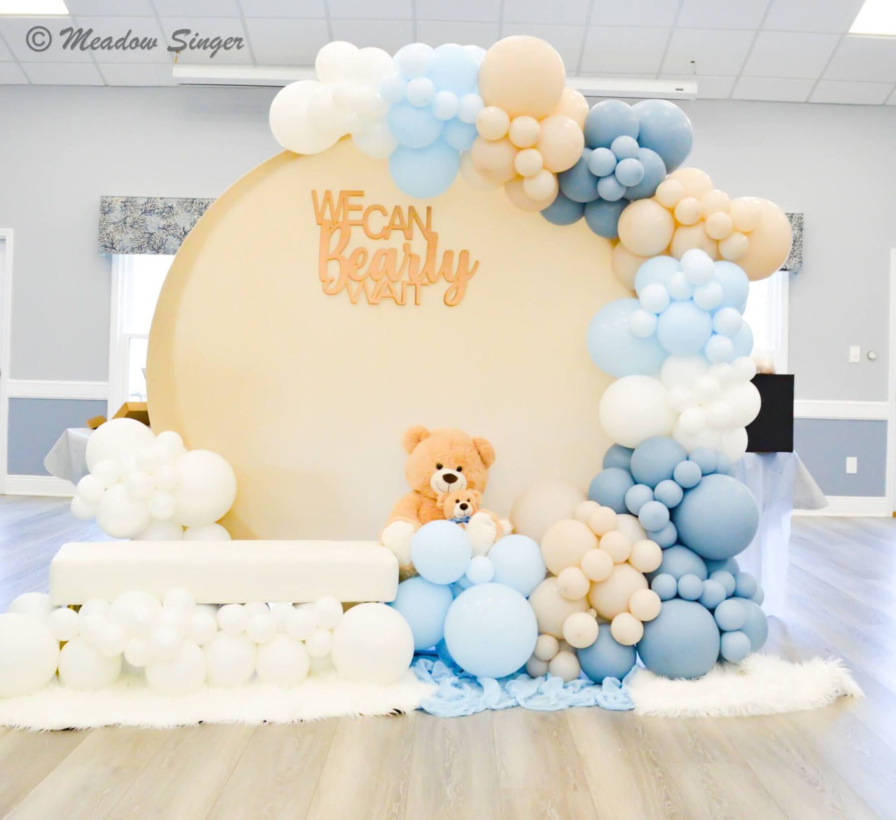 A cream balloon arch with teddy bears set up for a baby shower