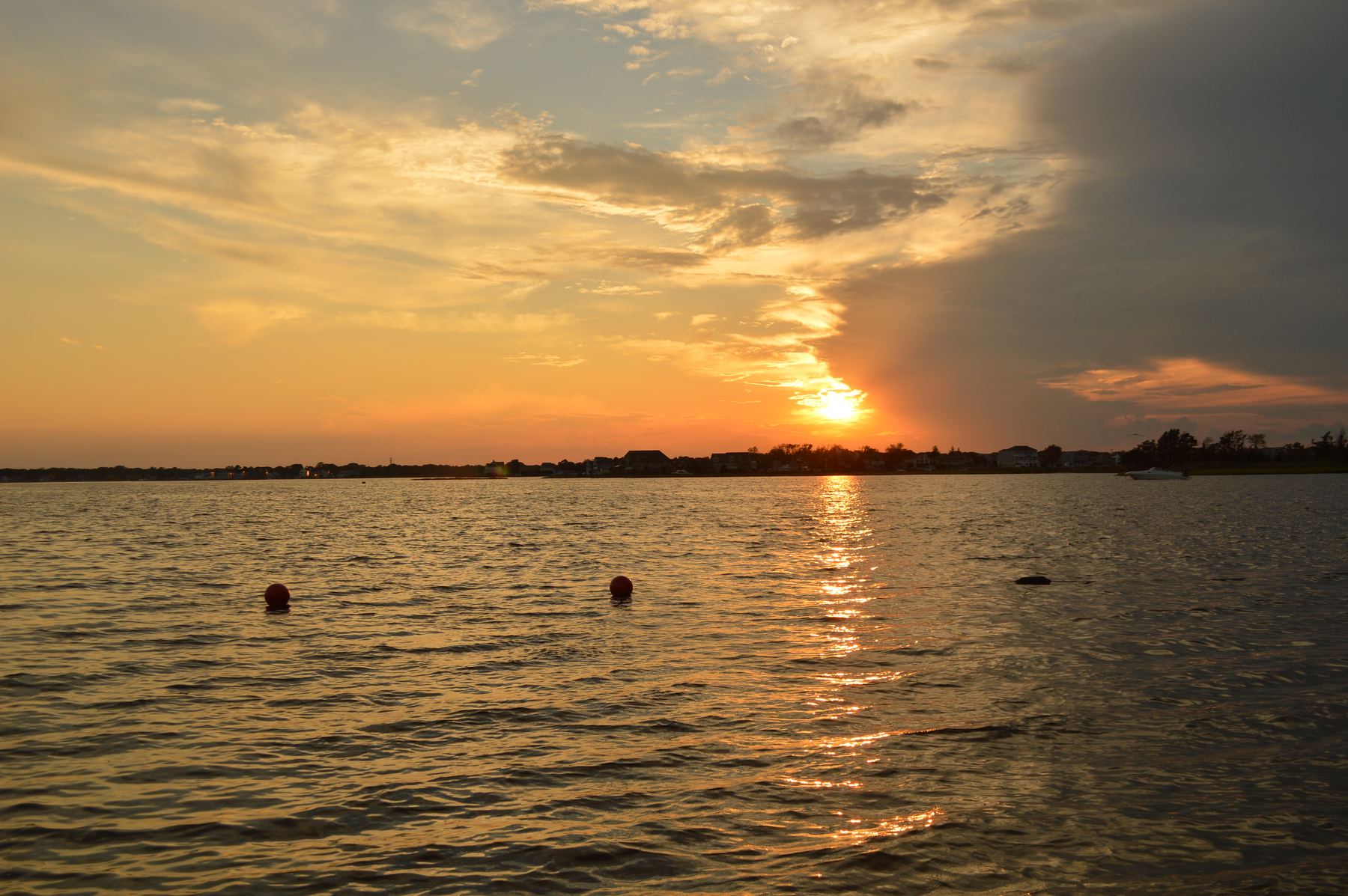 The sun setting over a calm bay under orange clouds